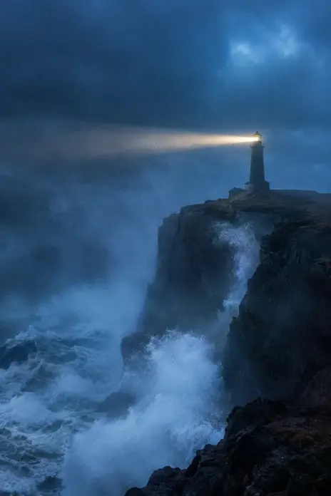 Image made with GPT Image 2.5 Flare: A lone lighthouse on a basalt cliff during a violent storm at blue hour, waves exploding i